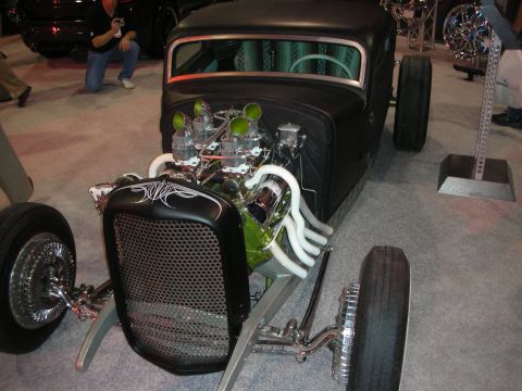1998 Ford Crown Victoria - Flat-black traditional hot rod with an exposed V8, dual carburetors and white wrapped headers displayed at an indoor show.
