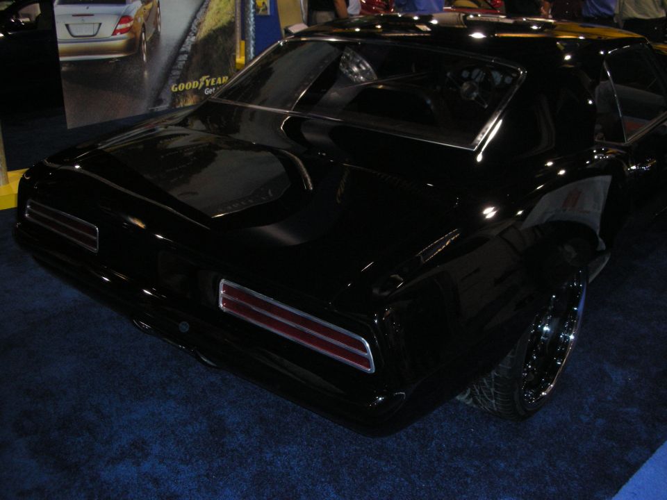 Rear of a glossy black muscle car coupe with split taillights on a blue carpet