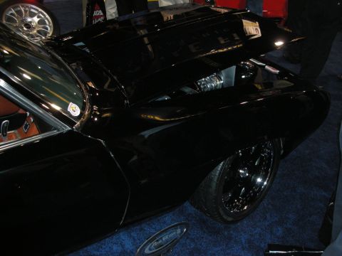 1998 Ford Crown Victoria - Side-front view of a glossy black custom car with a raised cowl hood and black wheels on a blue show carpet.
