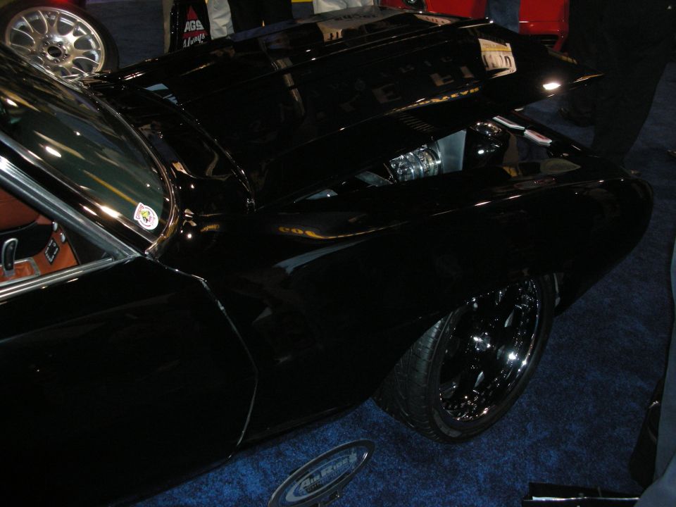 Glossy black custom car with cowl-induction hood and black wheels on blue carpet