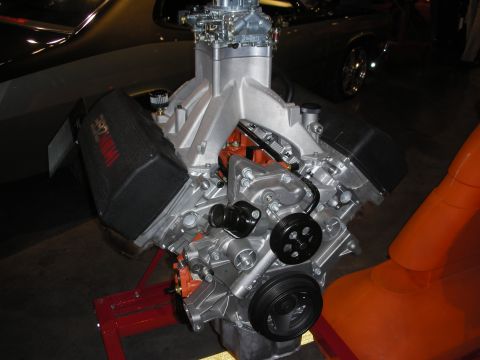 1998 Ford Crown Victoria - bare aluminum V8 crate engine with a single carburetor mounted on a red engine stand at a show.