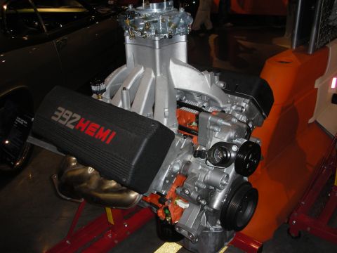 1998 Ford Crown Victoria - 392 Hemi crate engine on a red stand, its black valve cover lettered 392 HEMI, shown at an indoor display.