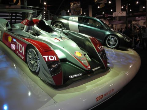 1998 Ford Crown Victoria - Audi R10 TDI prototype racer with Shell and Michelin livery sits on display next to a green Audi R8 coupe.