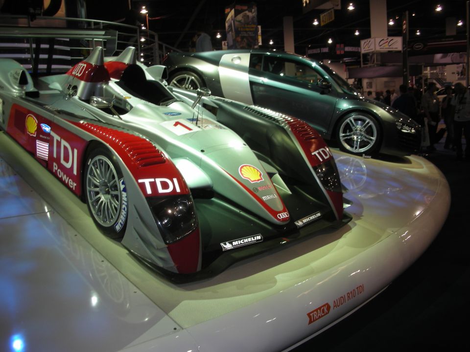 Audi R10 TDI Le Mans prototype race car beside a green R8 coupe at a show