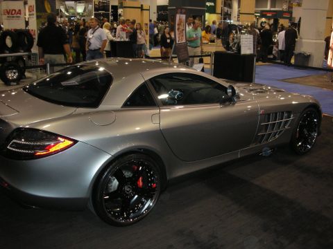 1998 Ford Crown Victoria - silver Mercedes-Benz SLR McLaren coupe with black multi-spoke wheels sits on a show floor amid booths and attendees.