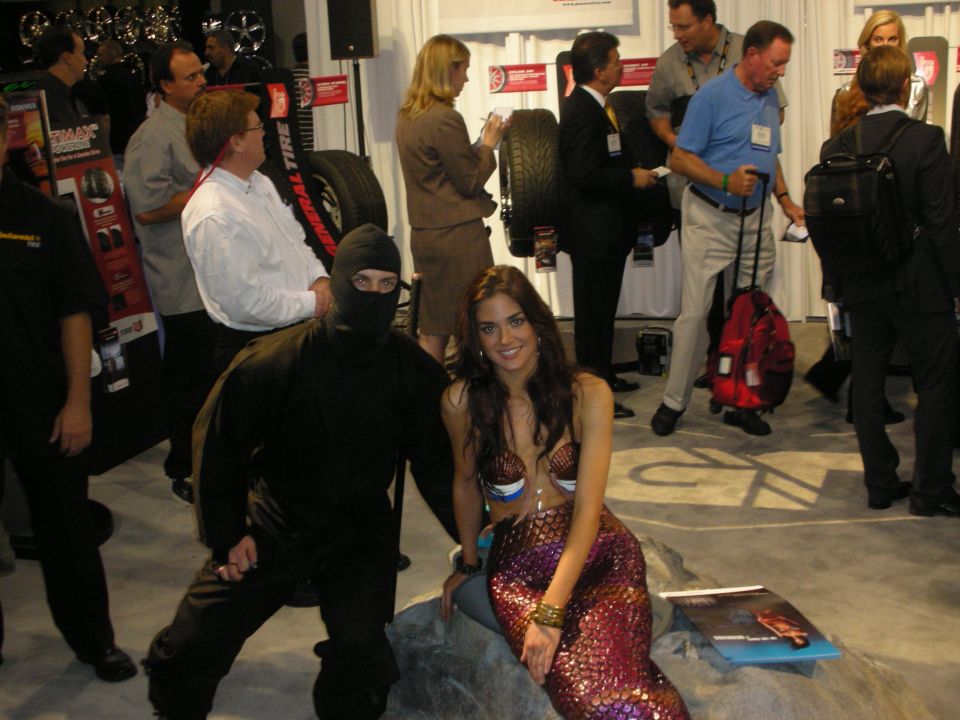 Person in black ninja outfit and woman in sequined mermaid costume at a tire booth