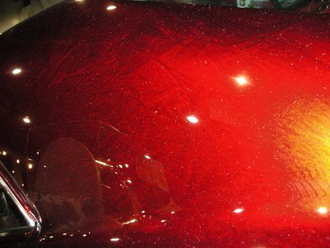 1998 Ford Crown Victoria - extreme close-up of glossy metallic-red car paint reflects overhead booth lights and a shimmering flake finish.