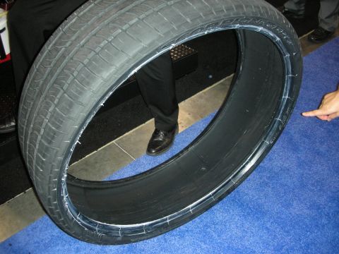 1998 Ford Crown Victoria - oversized low-profile performance tire stands upright on blue show carpet as a hand points to its sidewall.