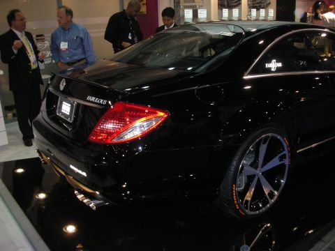 1998 Ford Crown Victoria - black Mercedes-Benz CL coupe with chrome multi-spoke wheels sits on a glossy show floor as attendees talk nearby.