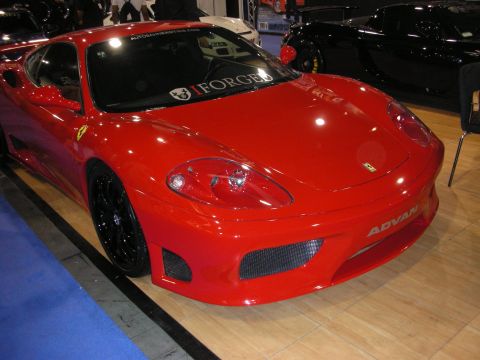 1998 Ford Crown Victoria - red Ferrari 360 Modena coupe with black wheels and Advan and Forged decals sits on a show floor beside a dark sports car.