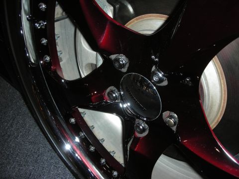 1998 Ford Crown Victoria - Close-up of a glossy black and candy-red five-spoke alloy wheel with chrome lug bolts over a slotted brake rotor.