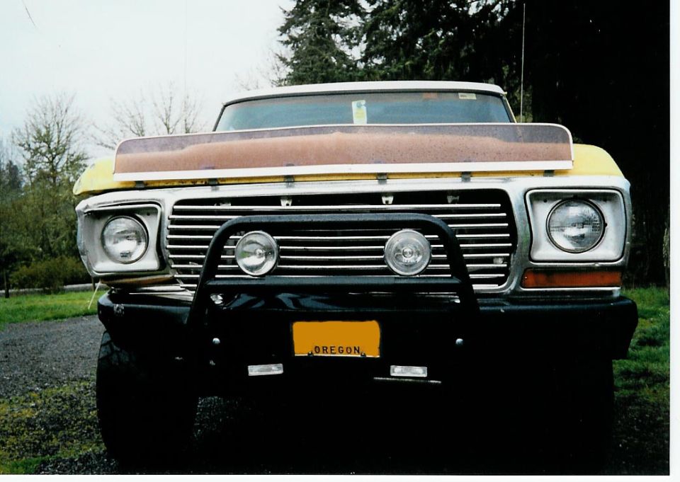 Front view of yellow Ford truck with brush guard, aux lights, primer hood, and Oregon plate