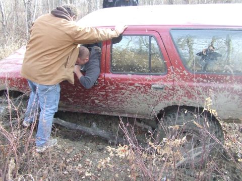 1990 Ford Bronco - People attempt to free a mud-covered red SUV from a ditch.
