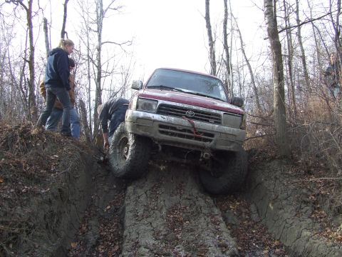 1990 Ford Bronco - Off-roading vehicle navigating a difficult muddy terrain with assistance from bystanders.