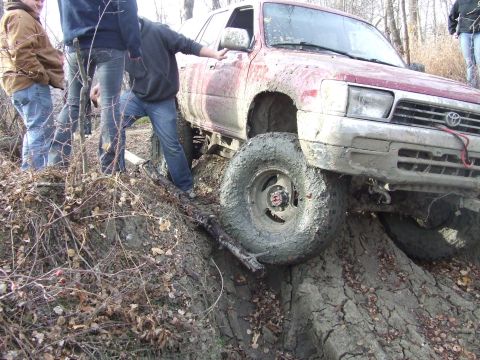 1990 Ford Bronco - A group of people watch as a mud-covered Toyota 4Runner navigates a challenging off-road obstacle.