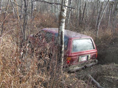 1990 Ford Bronco - A red SUV is stuck in a muddy ditch surrounded by trees and brush.