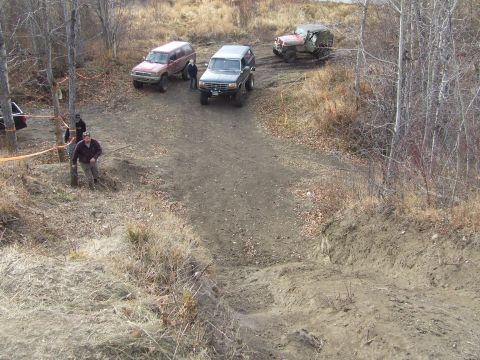 1990 Ford Bronco - Several SUVs and a jeep navigate a challenging dirt path in a wooded area.