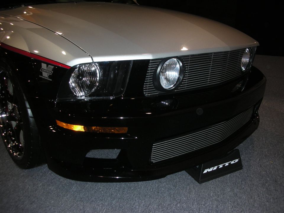 Front corner of a black and silver Mustang with billet grille and round headlights at an auto show