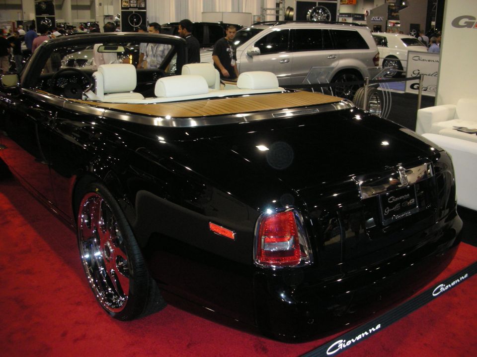 Rear of a black Rolls-Royce drophead convertible with teak deck and chrome wheels on a red show floor