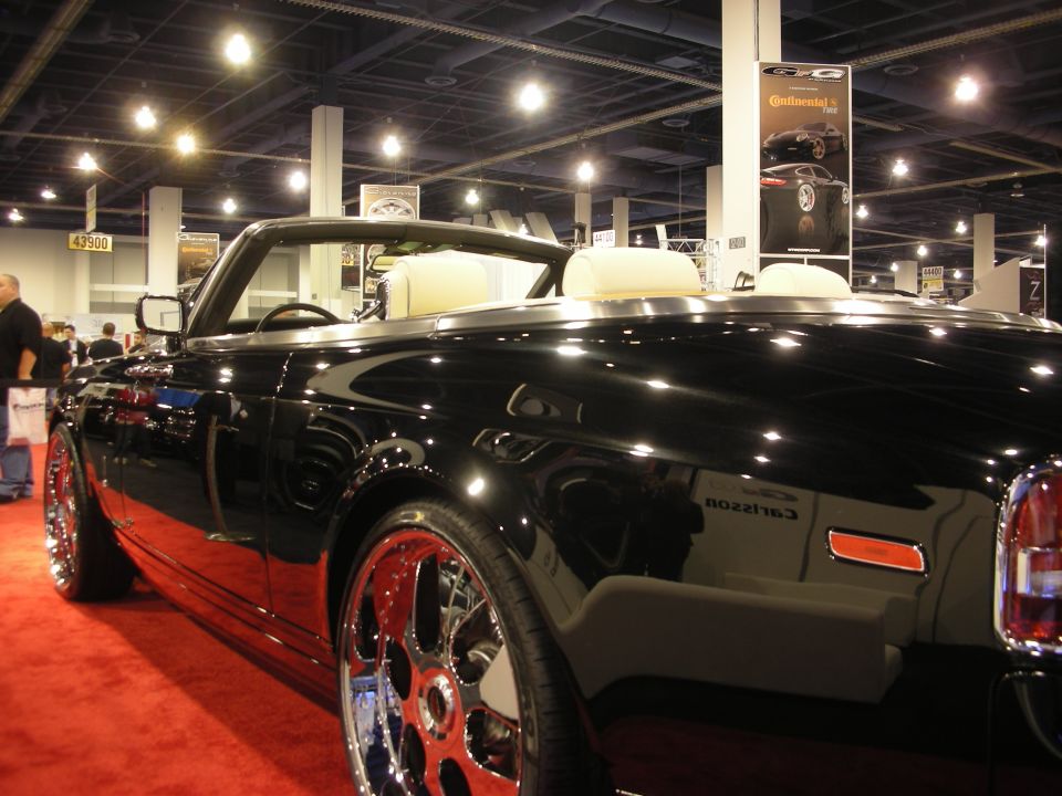 Side of a black convertible with chrome wheels and Carlsson script at an auto show on red carpet