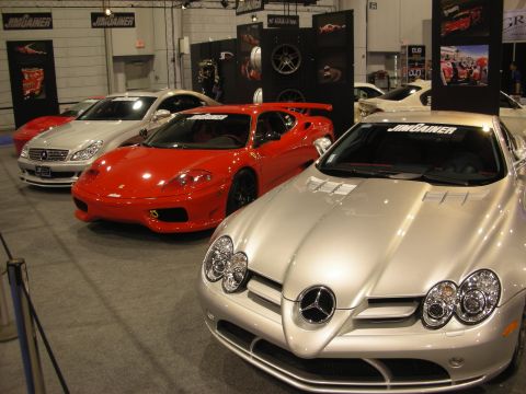 1998 Ford Crown Victoria - silver Mercedes-Benz SLR, a red Ferrari and a silver coupe lined up at an indoor auto show display booth.