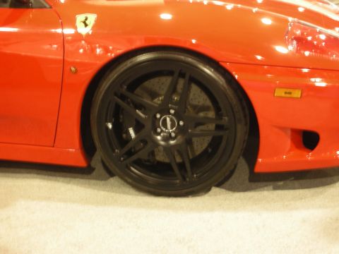 1998 Ford Crown Victoria - Close-up of a red Ferrari's front fender showing a matte black five-spoke wheel and the prancing-horse badge.