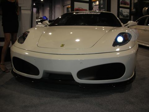 1998 Ford Crown Victoria - Front view of a white Ferrari F430 with black lower intakes and one headlight illuminated at an auto show.