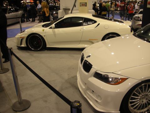 1998 Ford Crown Victoria - white Ferrari coupe behind a rope stanchion sits beside the front end of a white BMW at an auto show.