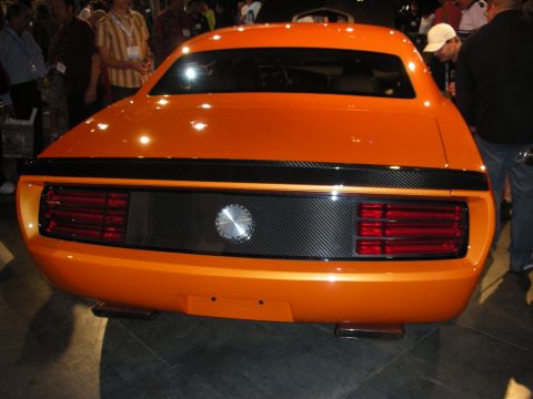 1998 Ford Crown Victoria - Rear view of an orange muscle-style coupe with a carbon-fiber rear panel and round taillights amid an auto show crowd.