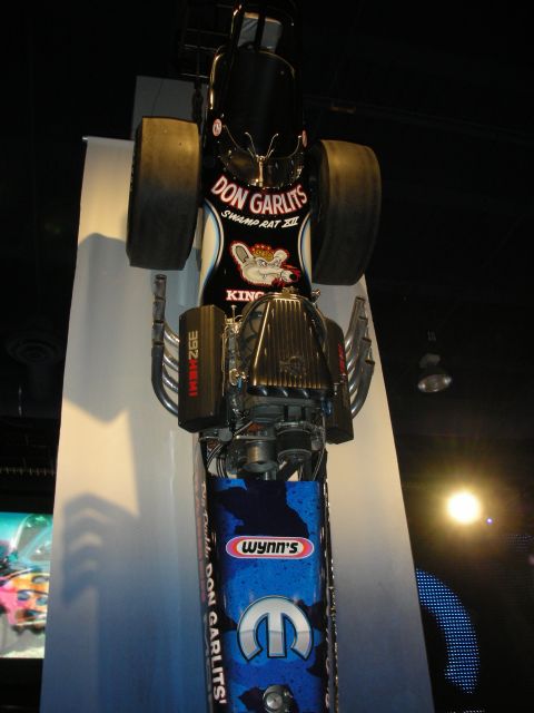 1998 Ford Crown Victoria - vertically mounted Don Garlits 'Swamp Rat' dragster in Wynn's and Mopar livery displayed against a blue wall.