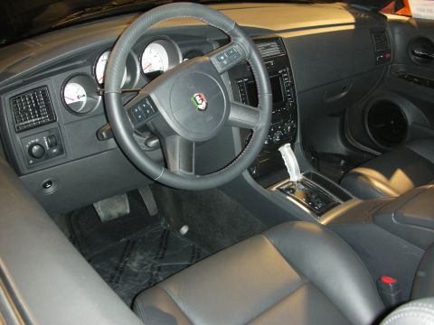 1998 Ford Crown Victoria - Black leather interior showing round gauges, a console shifter and a crest emblem on the steering wheel hub.