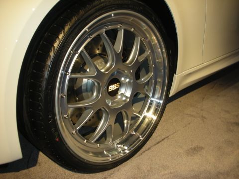 1998 Ford Crown Victoria - polished BBS split-spoke wheel with gold center badge mounted on a white vehicle over carpeted show flooring.