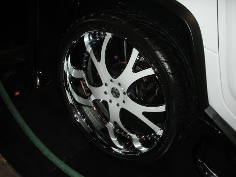 1998 Ford Crown Victoria - large chrome-lipped seven-spoke wheel with white spokes mounted on a white SUV at an indoor display.