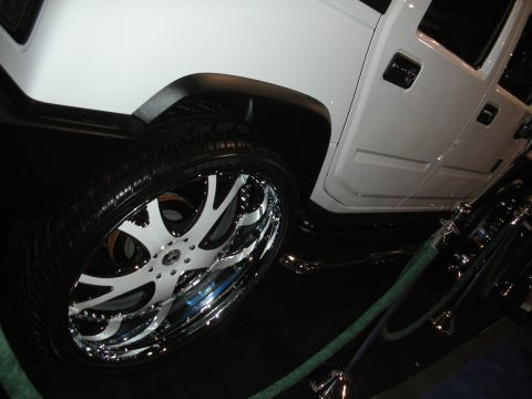1998 Ford Crown Victoria - white Hummer-style SUV with an oversized chrome-and-white custom wheel displayed behind a green stanchion rope.