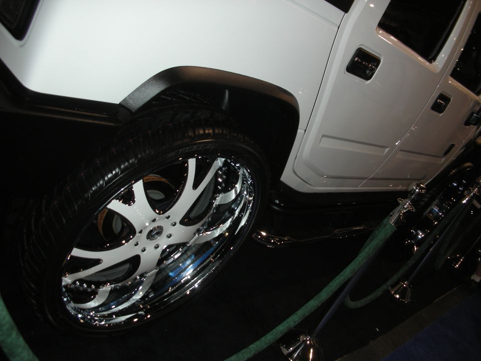 White Hummer with large chrome and white custom wheel behind a green rope