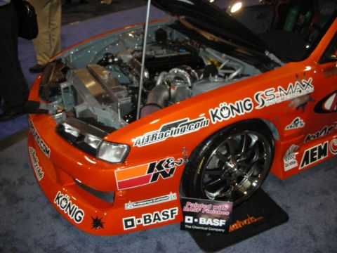 1998 Ford Crown Victoria - orange race car with its hood up showing the engine, covered in Konig, K&N, AEM and BASF sponsor decals.