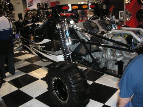 1998 Ford Crown Victoria - black tube-frame off-road sand rail buggy with long-travel coilovers and paddle tires displayed on a checkered floor.