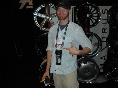 1998 Ford Crown Victoria - smiling bearded man in a ball cap and lanyard points at his BUYER badge while standing before a wall of display wheels.
