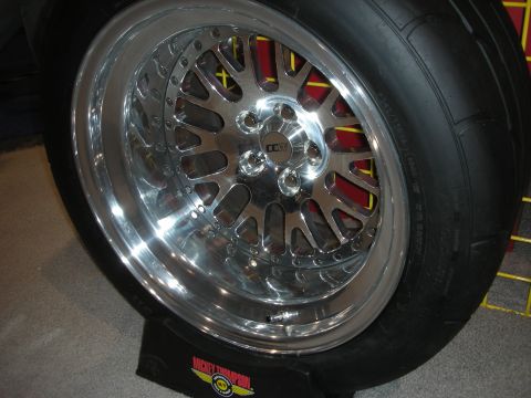 1998 Ford Crown Victoria - polished mesh-pattern bolt-together drag wheel fitted with a wide slick tire on a Mickey Thompson display stand.