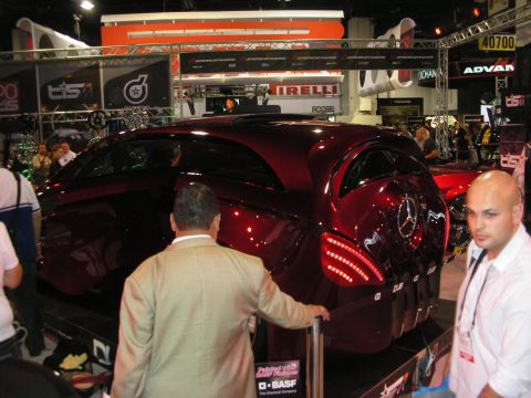 1998 Ford Crown Victoria - deep-red custom retro-styled coupe with LED taillights on a show stand as several onlookers gather around it.