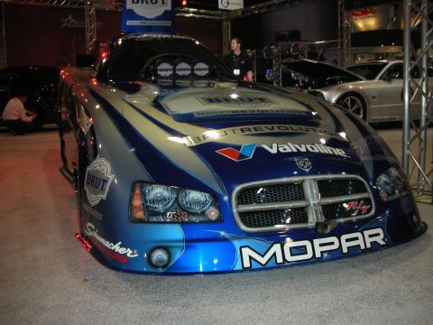 1998 Ford Crown Victoria - blue Dodge Charger-bodied drag race car with Mopar, Valvoline and Brut sponsor livery displayed under show lighting.