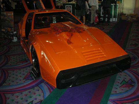 1998 Ford Crown Victoria - orange custom sports car with a raised gullwing door and louvered hood sits on patterned casino-style carpet.