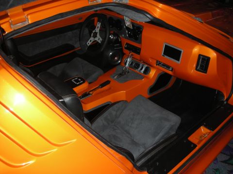 1998 Ford Crown Victoria - Custom interior of an orange sports car showing black suede seats, a three-spoke wheel and a small dashboard screen.