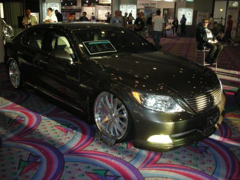 1998 Ford Crown Victoria - dark gray Lexus LS sedan sits lowered on large chrome wheels under show lighting at an indoor exhibition.