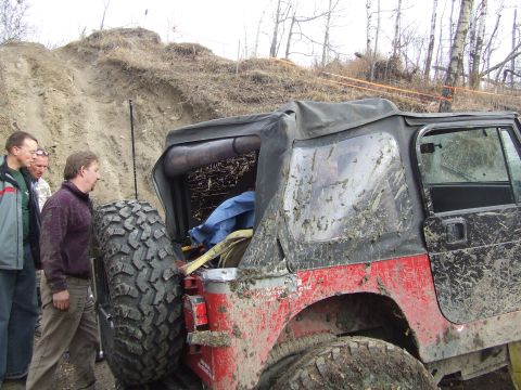 1990 Ford Bronco - A muddy red Jeep Wrangler with a soft top is parked on an off-road trail while people observe.