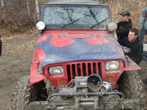 1990 Ford Bronco - A red and blue camouflage Jeep Wrangler is stuck in the mud, with two people standing nearby.