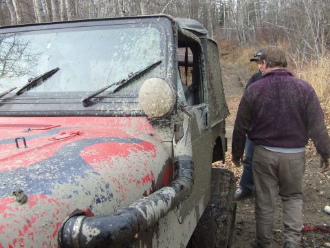 1990 Ford Bronco - Muddy Jeep Wrangler with snorkel attachment on a trail with two people walking away.