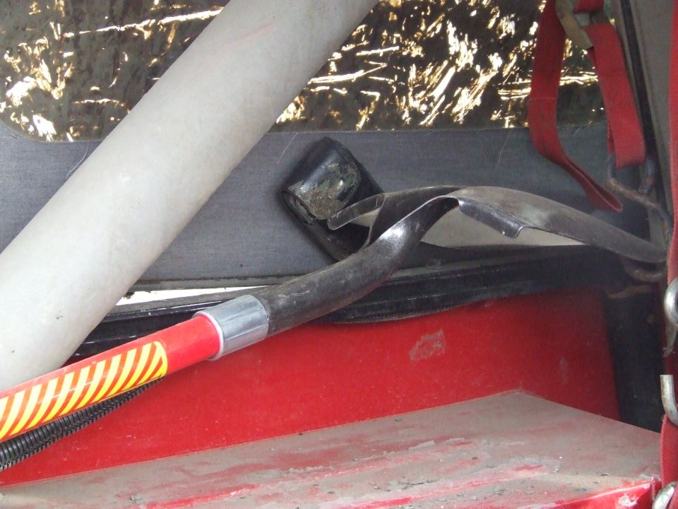 Shovel with red and yellow striped handle resting on red interior surface next to a white roll bar