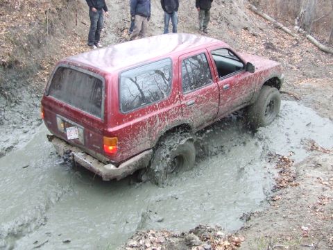 1990 Ford Bronco - Red SUV struggling in deep mud during an off-road excursion.