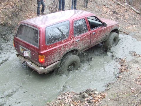 1990 Ford Bronco - This red SUV is struggling to get through a deep mud pit on an off-road trail.